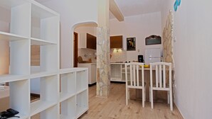A modern kitchen with white cabinets, a dining table with chairs, and a stone accent wall. - Studio apartment 1364/12839 (Istria - Pula), 2500m from the beach (Pula)
