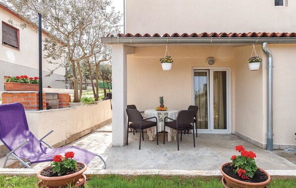 Une terrasse extérieure avec une table et des chaises, des plantes en pot et un fauteuil violet.