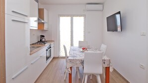 Une cuisine compacte dotée d’appareils électroménagers modernes, un coin repas avec une table et des chaises, et un téléviseur fixé au mur.