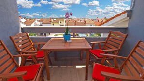 Un balcon avec une table en bois et quatre chaises, un pot de fleurs et une vue sur des bâtiments en arrière-plan.