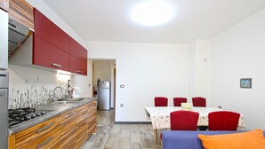 A compact kitchen with modern appliances, a dining area with a table and chairs, and a sofa with a cushion.