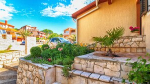 A stone staircase leading to a building with a yellow exterior, surrounded by lush greenery and a clear blue sky.