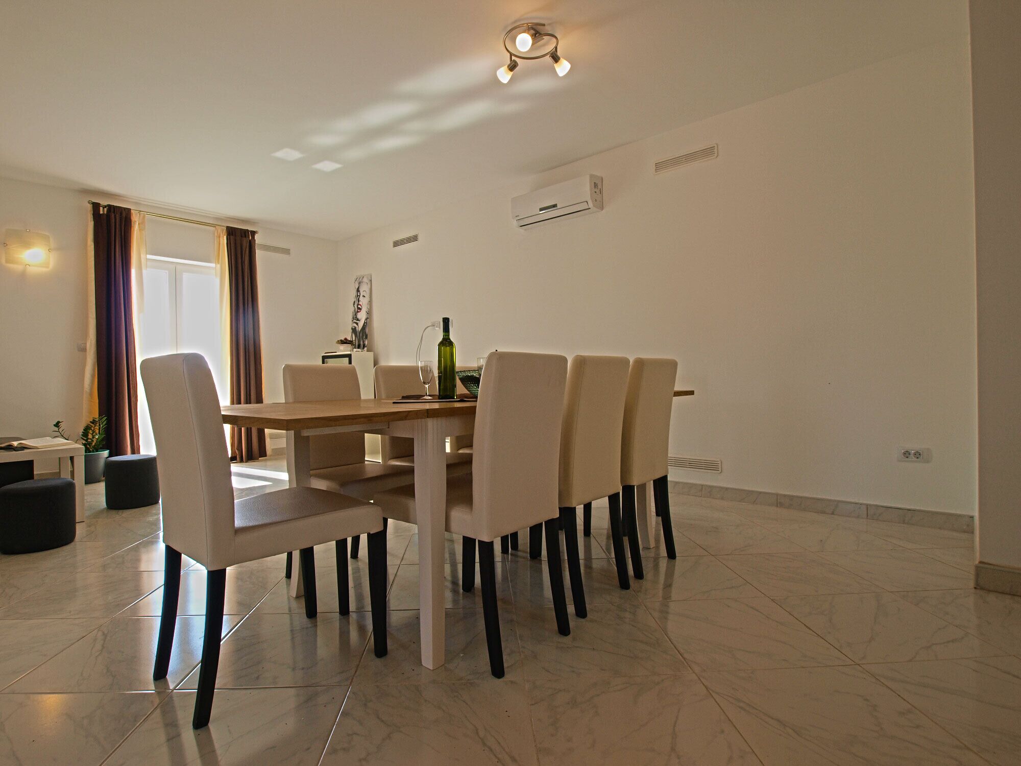 Un coin repas moderne avec une table en bois et six chaises. On peut voir une plante en pot sur le sol, à gauche.