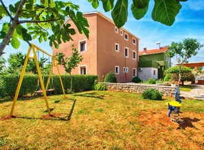 Un immeuble d’habitation à la façade rouge, doté d’une aire de jeux avec des balançoires et d’un petit jardin.