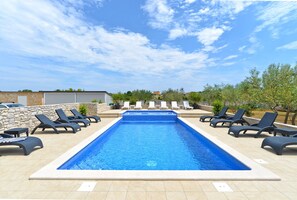 Une piscine rectangulaire, bordée d’une terrasse carrelée, entourée de chaises longues et de plantes en pot.