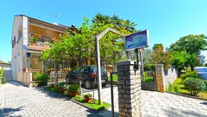 A residential building with a paved driveway, a parked car, and a stone wall with a sign. - Apartment 1377/13012 (Istria - Poreč), 800m from the beach (Poreč)