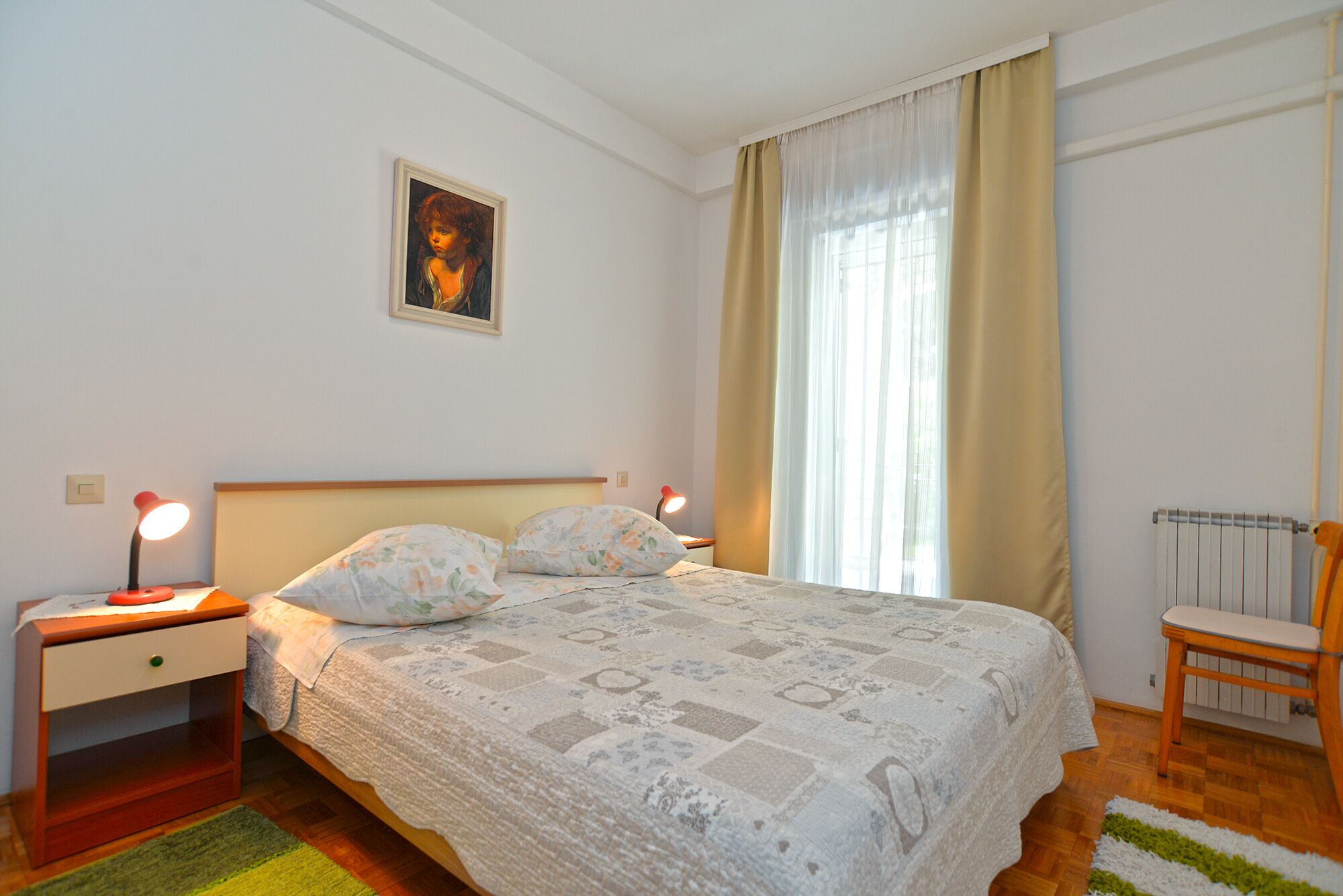 Une chambre à coucher avec un lit, des tables de chevet, une chaise, un radiateur et un tableau accroché au mur.