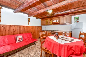 Una stanza accogliente con un divano rosso, un tavolo da pranzo in legno e un angolo cottura con mobili in legno.