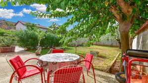An outdoor patio with a round table and four red chairs, surrounded by greenery and a tree. - House 1378/12993 (Istria - Galižana), 7500m from the beach (Galižana)
