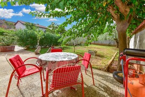 Un patio esterno con un tavolo rotondo e quattro sedie rosse, immerso nel verde e con un albero.