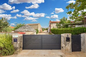 Una entrada protegida por un muro de piedra y una reja metálica, que conduce a un camino.