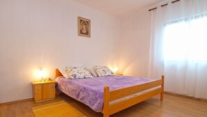 A bedroom with a wooden bed, two bedside tables with lamps, a small rug, and a window with curtains.