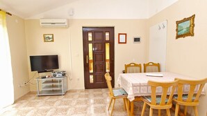 A room with a television on a stand, a dining table with chairs, a wooden door, and a tiled floor. - Apartment 1390/13114 (Istria - Valbandon), 700m from the beach (Valbandon)