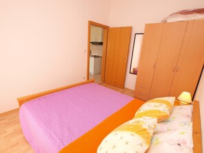 A bedroom with a bed, a wardrobe, and a small kitchenette in the background.