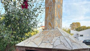 A stone-built outdoor pizza oven with a brick base and a chimney.