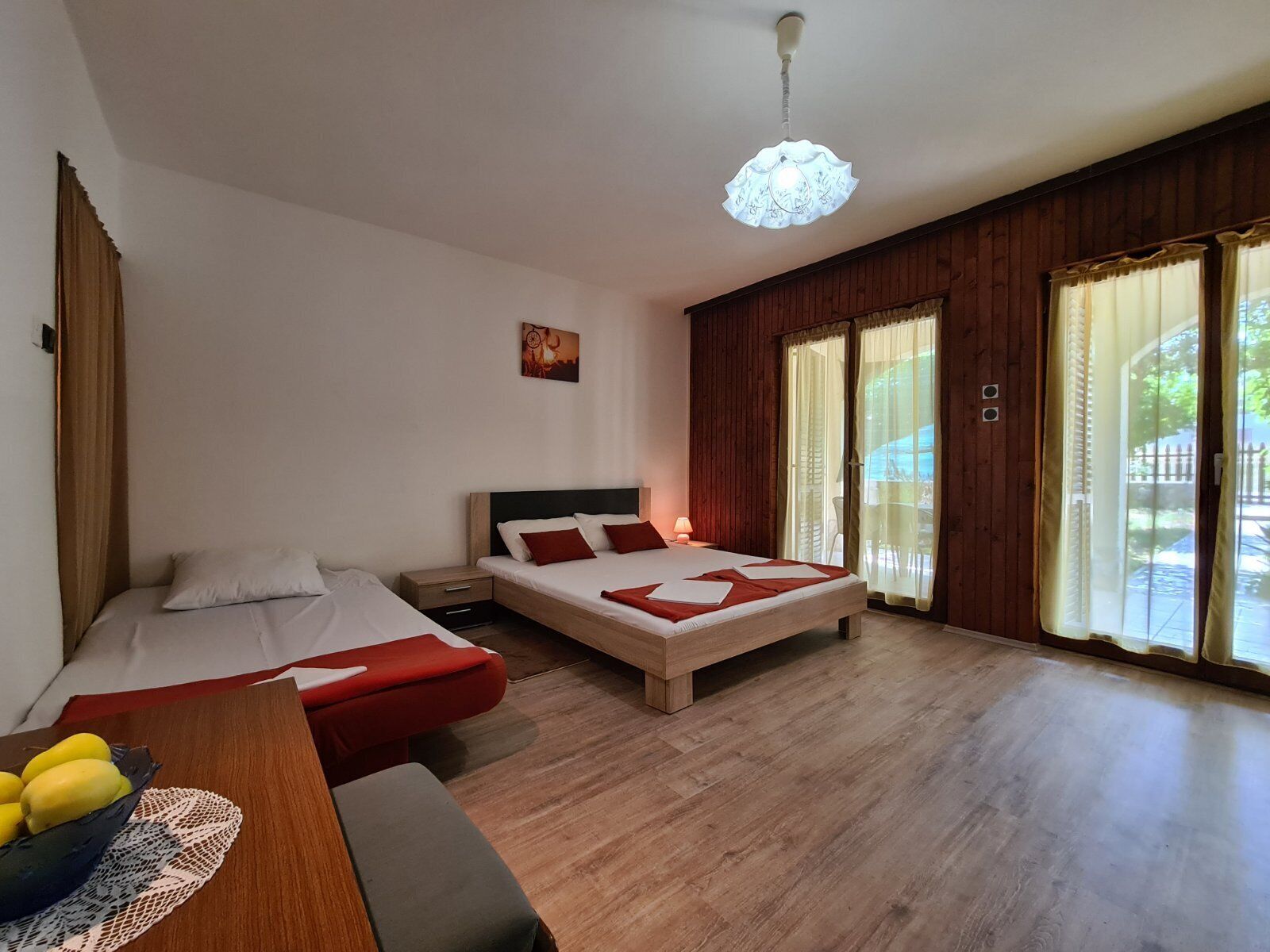 Un dormitorio con dos camas, suelo de madera, un escritorio con un cuenco de fruta y una ventana con cortinas.