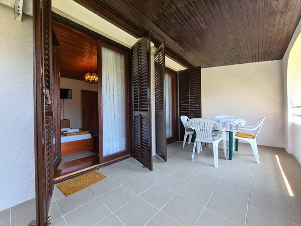 A room with a bed, a small table with chairs, a wooden ceiling, and a view of the outside.
