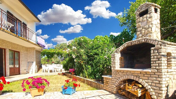 A stone-built outdoor kitchen with a chimney, surrounded by a garden with flowering plants and a paved patio. - Apartment 1398/13153 (Istria - Pjescana Uvala), 350m from the beach (Pjescana Uvala)