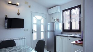 A compact kitchen with a refrigerator, a dining table with chairs, a TV mounted on the wall, and a window with curtains. - Apartment 1398/13155 (Istria - Pjescana Uvala), 350m from the beach (Pjescana Uvala)