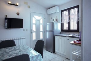 Uma cozinha compacta com geladeira, uma mesa de jantar com cadeiras, uma TV na parede e uma janela com cortinas.