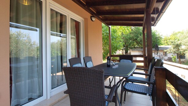 A covered patio with a table and chairs, large windows, and a view of the outdoors.
