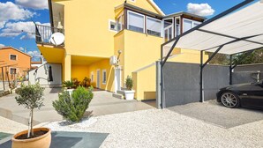 A yellow two-story house with a covered driveway, a satellite dish, and a car parked in the garage.