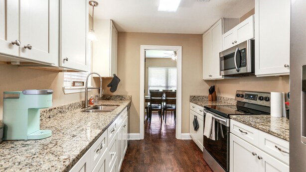 A kitchen with white cabinets, granite countertops, a built-in microwave, and a stove.
