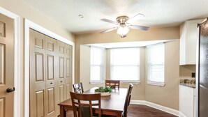 A dining area with a wooden table, chairs, a ceiling fan, and windows with blinds.