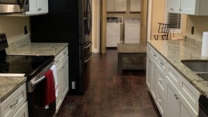 A kitchen with white cabinets, a black refrigerator, a microwave, and a stove. There is a ceiling fan and a window with blinds.