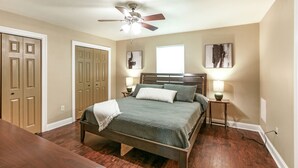 A bedroom with a bed, two bedside tables with lamps, a ceiling fan, and wooden doors.