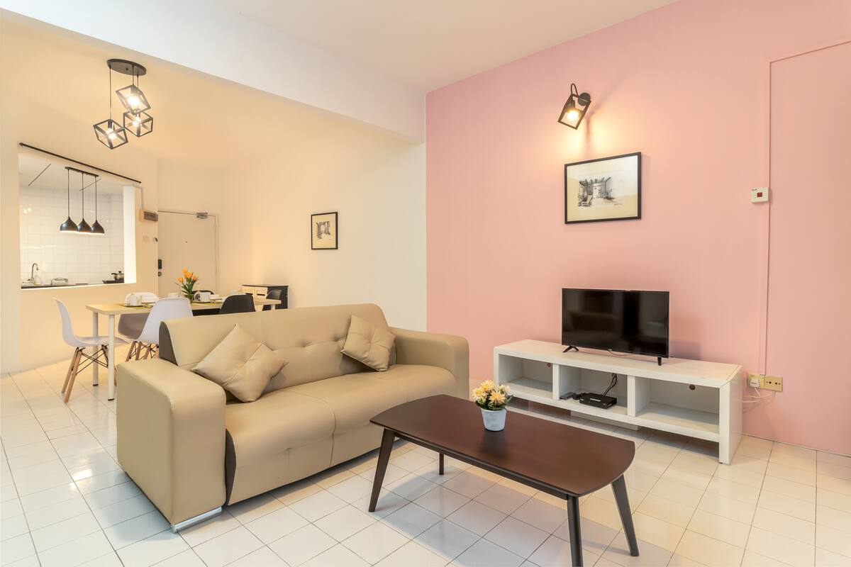 Ein modernes Wohnzimmer mit einem beigefarbenen Sofa, einem Couchtisch, einem Fernseher auf einem weißen Schrank und einer Wand in Rosé.