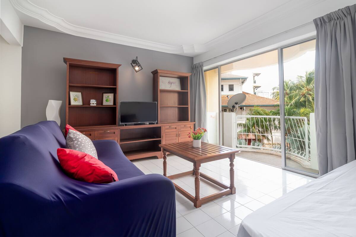 Ein modernes Wohnzimmer mit Sofa, TV-Schrank und einem Balkon mit Blick auf Palmen.