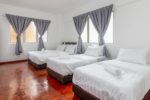 Three single beds with white bedding and dark headboards, set against a white wall.