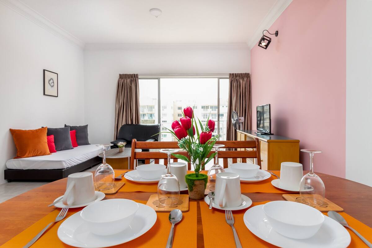 Ein Hotelzimmer mit Esstisch für vier Personen, einer Couch, einem Fernseher und einem Fenster mit Vorhängen.