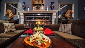 A cozy living room with a fireplace, two sofas, and a wooden coffee table with a fruit and cheese platter. - Grand Yazıcı Uludağ (Bursa)