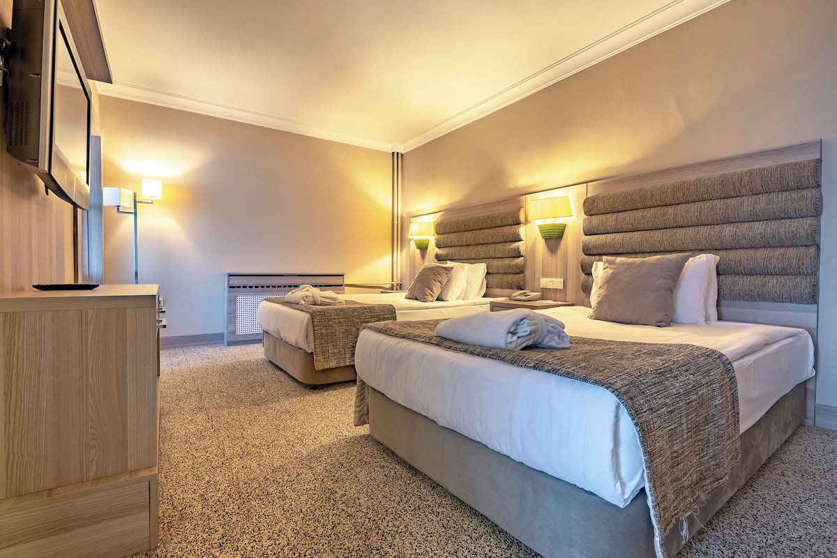 A hotel room with two beds, a wooden dresser, a mirror, and wall-mounted lamps.