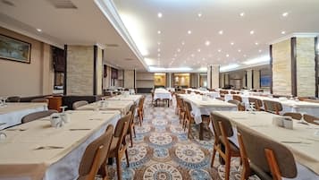 A spacious banquet hall with long tables, wooden chairs, and a patterned carpet.