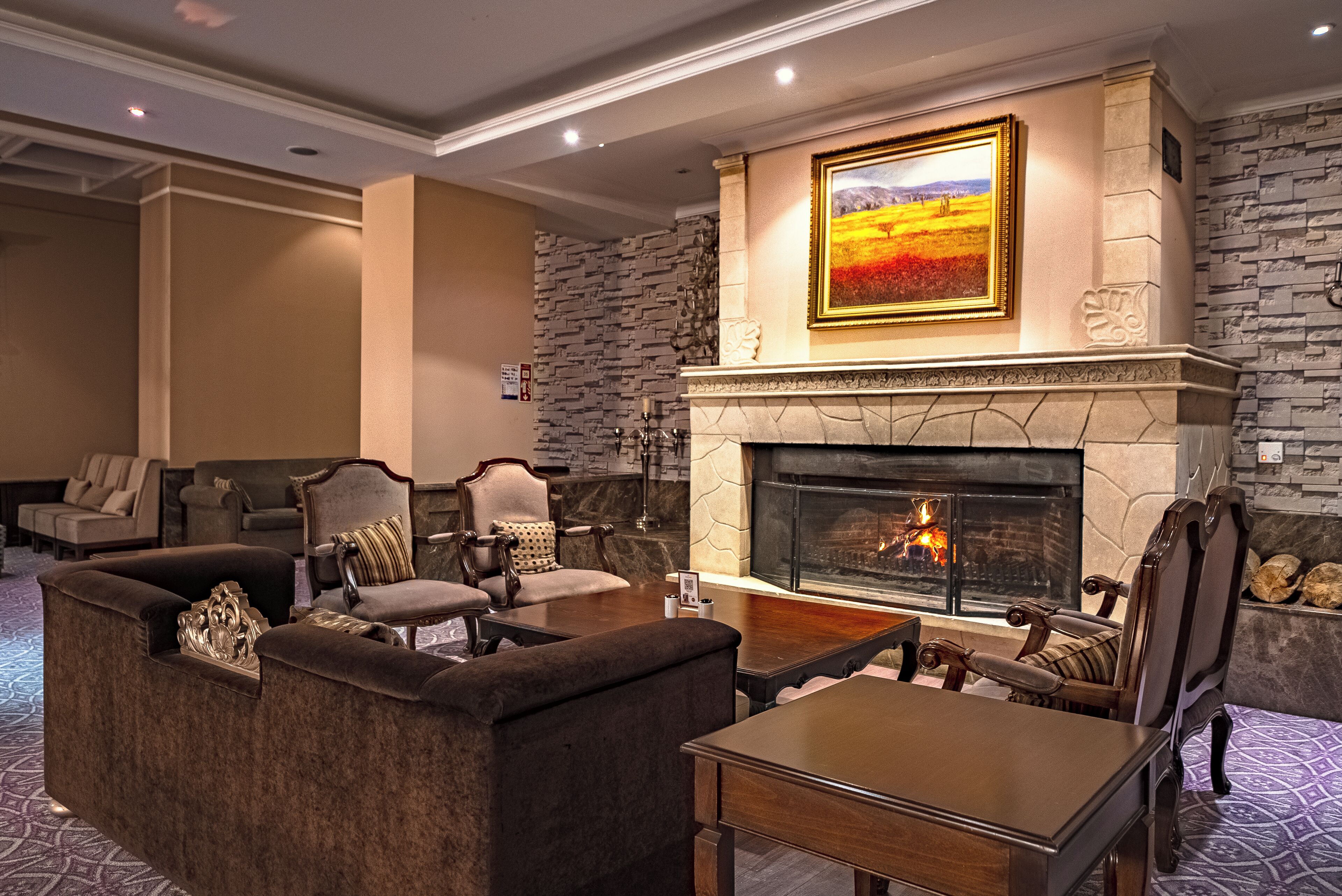 A cozy lounge area with a fireplace, comfortable seating, and a large painting above the mantel.