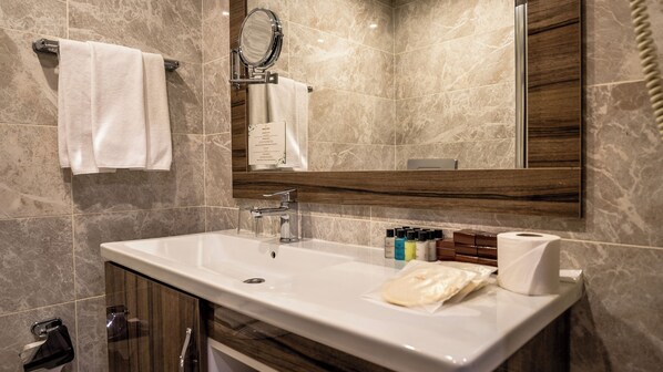 A bathroom with a marble-tiled wall, a white sink, a mirror, and a wooden vanity. - Grand Yazıcı Uludağ (Bursa)