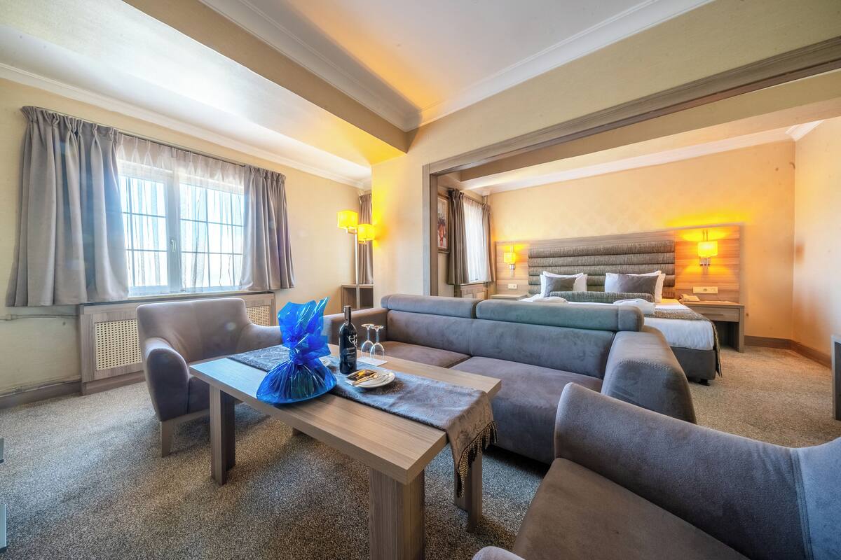 A hotel room with a sofa, a dining table, a bed, and a nightstand.