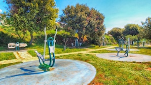 A park with exercise equipment, benches, and trees.