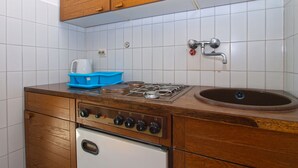 A compact kitchen with wooden cabinets, a gas stove, a sink, and a white refrigerator.