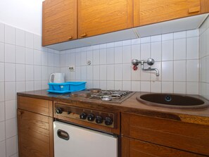 Cozinha compacta com armários de madeira, fogão a gás, pia e geladeira branca.