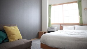 A hotel room with a bed, a small bedside table, a wall-mounted heater, and a window with curtains. - The Stay Wakkanai- Hostel (Wakkanai)