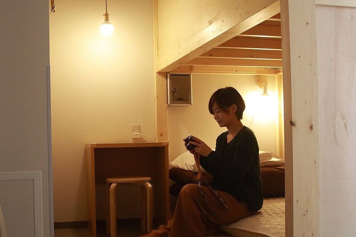 A person sitting on a bench in a room with a wooden ceiling, a small table, and a wall-mounted light.