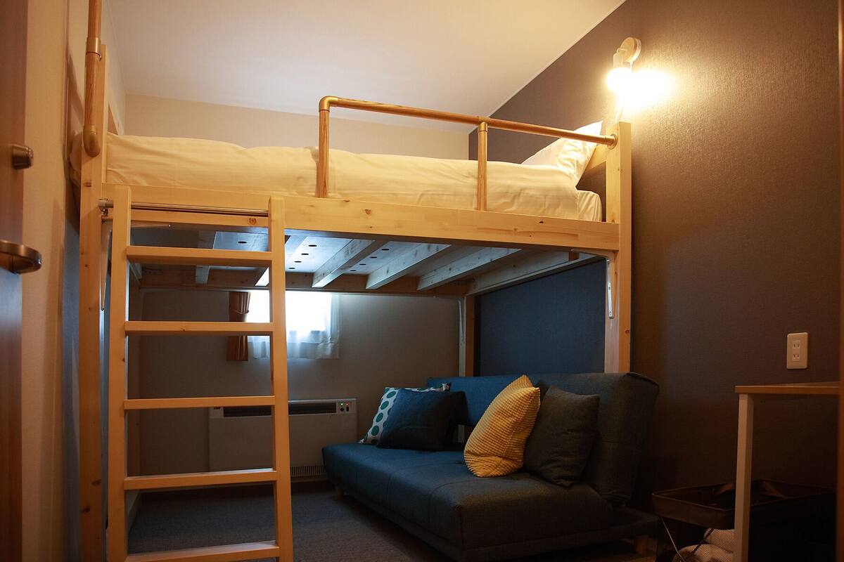 A compact room with a bunk bed, a sofa, and a ladder.