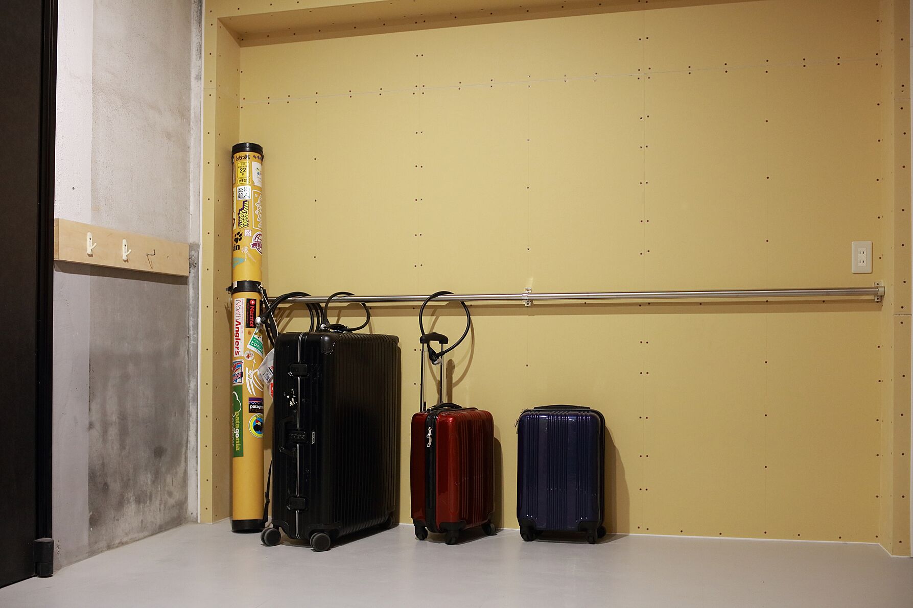 A luggage rack with three suitcases and a cylindrical object against a plain wall.