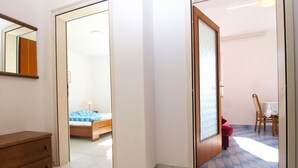 A room with a bed, a wooden dresser, and a door leading to another room with a table and chairs.