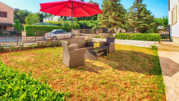 An outdoor patio with wicker furniture and a red umbrella.
