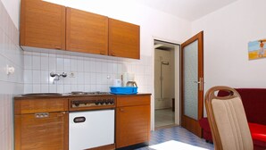 A compact kitchen with wooden cabinets, a stove, and a sink. There's a red sofa and a chair in the adjacent living area.